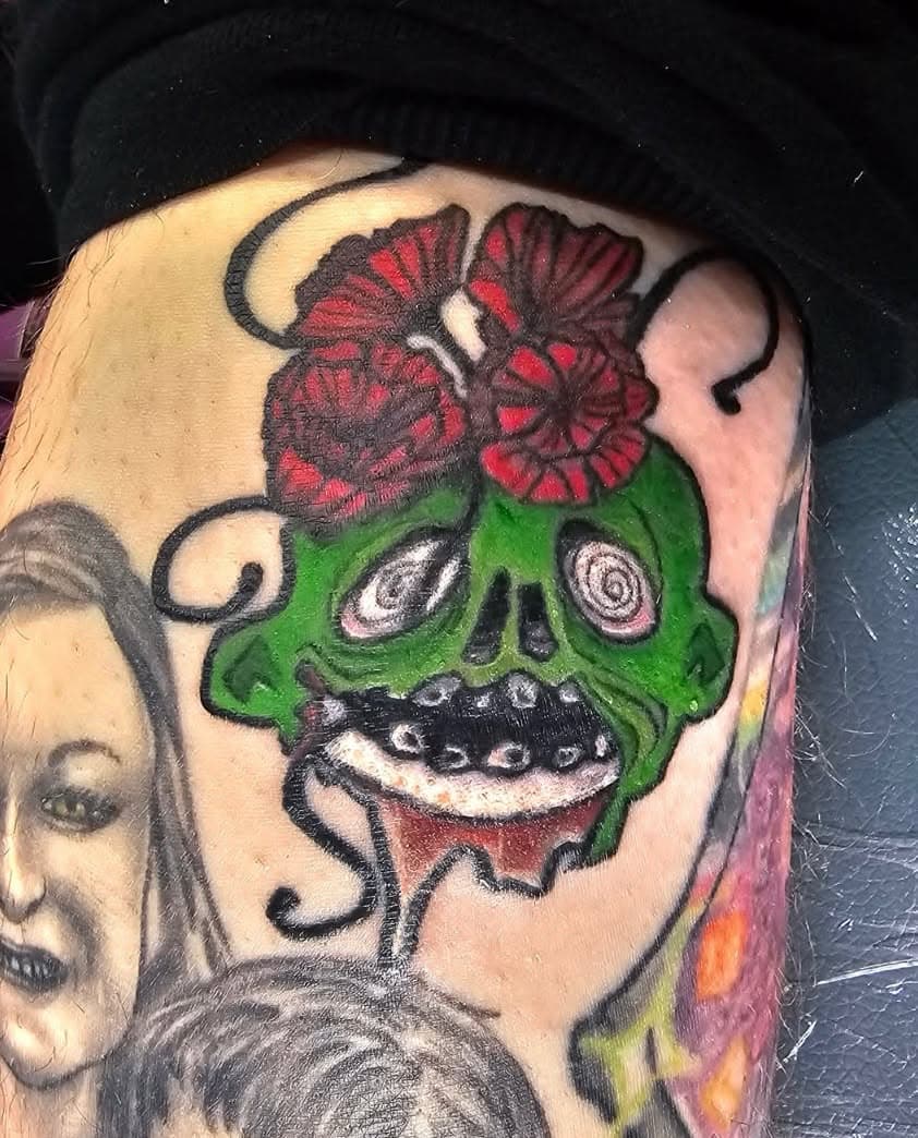 tattoo of a green rotting skull with poppies sprouting from the top